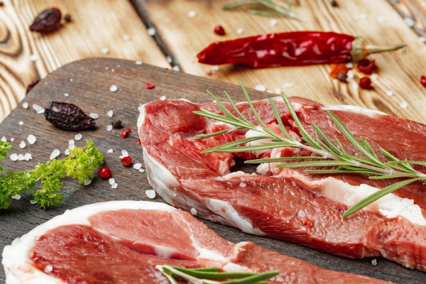 Raw meat steaks with herbs on wooden board