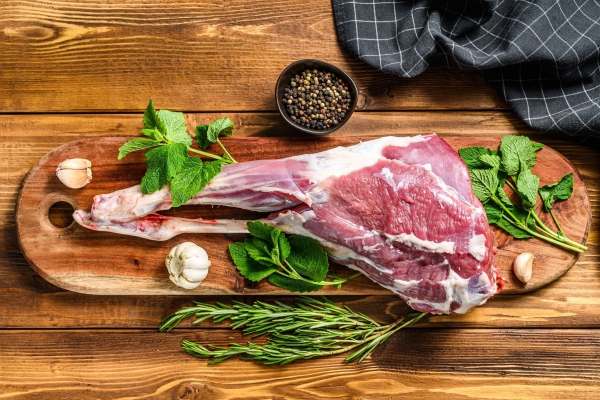 Sheep, lamb leg with herbs. Raw organic meat. Wooden background. Top view